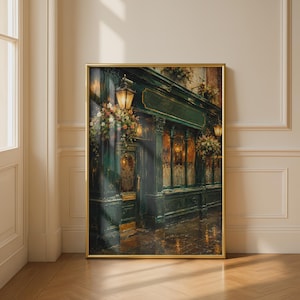 May include: A framed wall art print depicting the exterior of a dark green storefront at night. The scene features a glowing lantern, hanging flower baskets, and ornate glass windows. The artwork is encased in a thin gold frame and displayed.