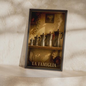 May include: A framed wall art print featuring five metallic stovetop espresso makers of varying sizes lined up on a wooden shelf. The image includes a small framed picture on the wall, hanging vines, and the text LA FAMIGLIA at the bottom.
