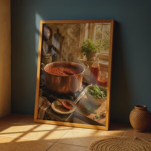 May include: A framed wall art print depicting a copper pot filled with red tomato sauce simmering on a stove. The scene includes a wooden spoon on a small plate, a glass bottle of sauce, a bowl of fresh green basil, and a window in the background.