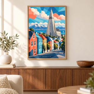 May include: A framed geometric art print of Reykjavik featuring the Hallgrimskirkja church, colorful houses, and snow-capped mountains under a blue sky with pink clouds. The word REYKJAVIK is printed in white at the bottom of the illustration.