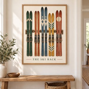 Op de afbeelding: Een ingelijste kunstdruk getiteld THE SKI RACK met een horizontaal houten rek met vijf paar vintage-stijl ski's in de kleuren groen, beige, blauw, geel en rood met diverse geometrische patronen en bindingen tegen een crèmekleurige achtergrond.