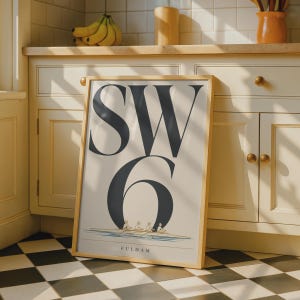 May include: A rectangular framed print featuring the large dark gray text SW 6 centered on a light background. Below the text is a detailed illustration of a four-person rowing crew in a boat on water, with the word FULHAM printed underneath.
