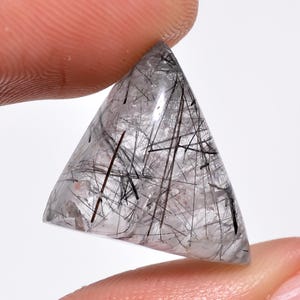 Peut inclure: Un cristal de quartz clair triangulaire et facetté avec des inclusions noires. Le cristal est translucide et a une texture naturelle et rugueuse.