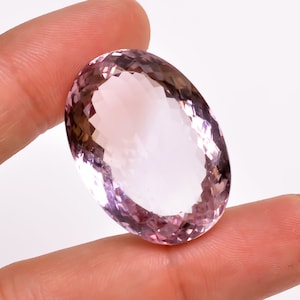 May include: A large, oval-shaped amethyst gemstone with a light purple hue. The gemstone is faceted and has a smooth, polished finish.