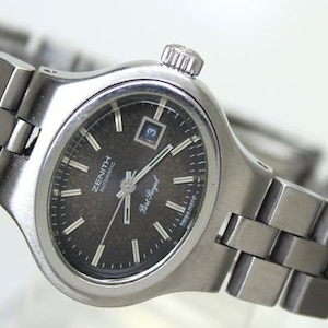 May include: A silver Zenith automatic wristwatch with a black face and a silver metal strap. The watch face has silver hands and markers, a date window, and the text "Zenith Automatic" and "Star Royal" printed on it.