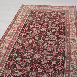 Peut inclure: Un tapis vintage avec un fond rouge foncé et un motif floral dans des tons de rose, blanc et beige. Le tapis a une bordure avec un motif géométrique.