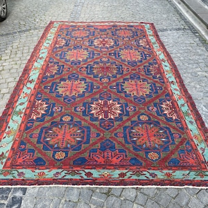 May include: A vintage Turkish rug with a geometric pattern in shades of red, blue, green, and orange. The rug has a light blue border with a floral design.
