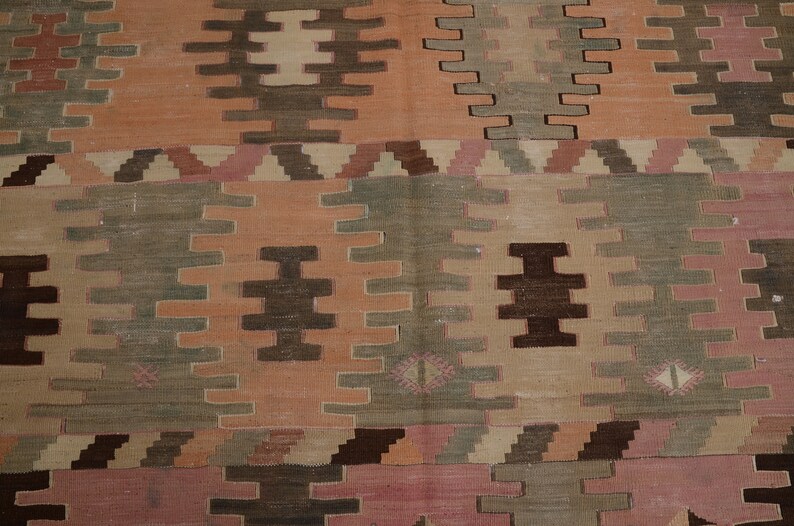 May include: A vintage rug with a geometric pattern in shades of brown, pink, and green. The rug has a worn and faded look, giving it a rustic and antique feel.