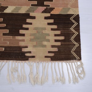 May include: A brown and beige patterned rug with a fringe border. The rug has a geometric design with a central diamond shape.