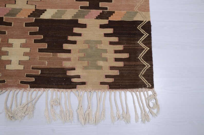 May include: A brown and beige patterned rug with a fringe border. The rug has a geometric design with a central diamond shape.
