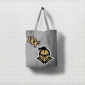 Pu&ograve; includere: Una borsa tote in tela grigia con un logo UCF Knights nero e oro. Il logo rappresenta un elmo da cavaliere con una visiera nera e una maschera facciale dorata.