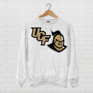 May include: A gray sweatshirt with the University of Central Florida logo. The logo features the letters "UCF" in black and gold with a knight's helmet in gold.