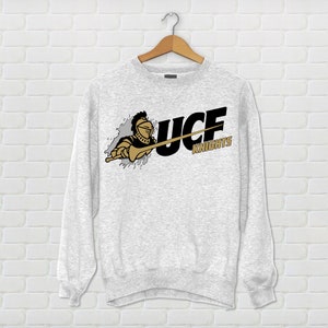 May include: A gray sweatshirt with a black and gold UCF Knights logo. The logo features a knight holding a sword and the words "UCF Knights".