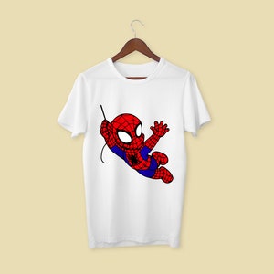 Puede incluir: Camiseta blanca con una imagen de dibujos animados de Spiderman en un traje rojo y azul balance&aacute;ndose en una telara&ntilde;a.