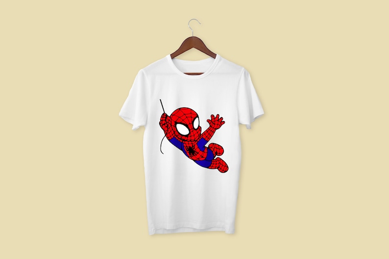 Puede incluir: Camiseta blanca con una imagen de dibujos animados de Spiderman en un traje rojo y azul balance&aacute;ndose en una telara&ntilde;a.
