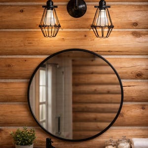 Puede incluir: Escena de baño rústico con un espejo redondo con marco negro, un lavabo de piedra y una encimera de madera. Encima del espejo, una lámpara de metal negro con dos lámparas tipo jaula cuelga de una pared de tablones de madera. Una pequeña planta en maceta y tarros están en la encimera.