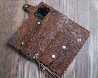 May include: A brown leather phone case with a floral embossed design. The case has a built-in wallet with multiple card slots and a money clip. The case also has a detachable wrist strap.
