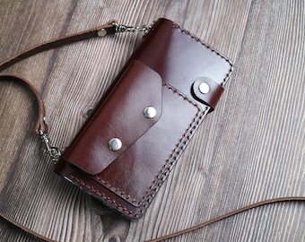 Pode incluir: Uma carteira de couro marrom com uma alça e uma corrente. A carteira tem vários bolsos e é costurada com um padrão decorativo.