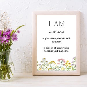 May include: A framed print with a white background and black text that reads "I AM a child of God. a gift to my parents and country. a person of great value because God made me." The bottom of the print features a border of colorful wildflowers.