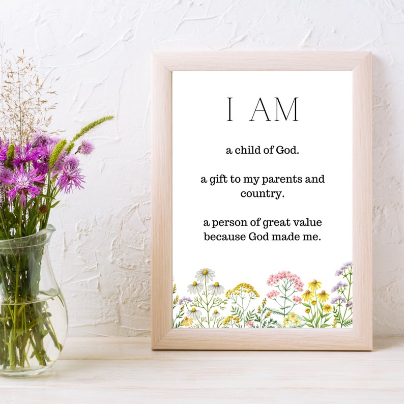 May include: A framed print with a white background and black text that reads "I AM a child of God. a gift to my parents and country. a person of great value because God made me." The bottom of the print features a border of colorful wildflowers.