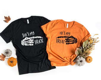 May include: Two black and orange t-shirts with a skeleton hand graphic and the text "She's my trick" and "He's my treat".