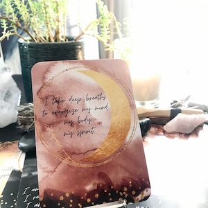 May include: A card with a gold crescent moon on a watercolor background with the text "I take deep breaths to energize my mind, my body, my spirit."