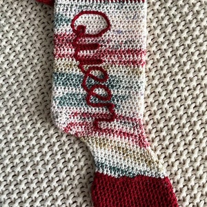 May include: A red and white striped crocheted Christmas stocking with the name "Olivia" embroidered in red.