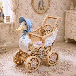Può includere: Una statuetta decorativa di un'anatra bianca con una cuffietta blu, integrata nella parte anteriore di una carrozzina beige decorata. La carrozzina presenta fianchi intagliati a forma di ala, accenti floreali color pastello e quattro ruote a forma di fiore.