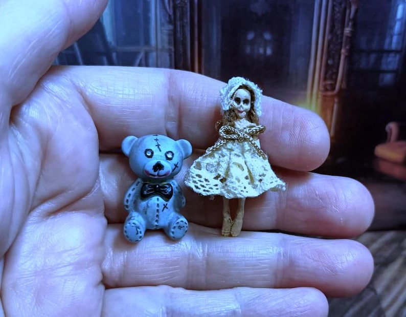 Puede incluir: Un peque&ntilde;o oso de peluche azul cosido con una pajarita negra y una mu&ntilde;eca de porcelana blanca con un vestido de encaje blanco.