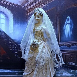 May include: A porcelain doll bride wearing a white lace wedding dress and veil. The doll is standing in a dark, gothic setting with a staircase and a painting of a ghost in the background.