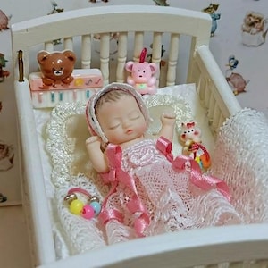 Może przedstawiać: Miniaturowa lalka w białym ł&oacute;żeczku, ubrana w r&oacute;żową sukienkę i czepek. Ł&oacute;żeczko ma białą ramę i jest ozdobione koronkowym kocykiem i małymi zabawkami, w tym misiem i r&oacute;żowym misiem. Tło przedstawia tapetę z ilustracjami zwierząt.