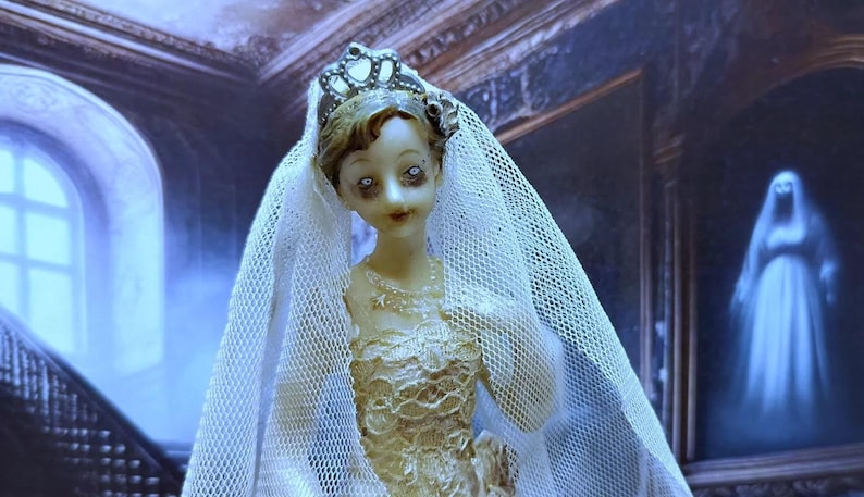 May include: A porcelain doll bride wearing a white veil and a gold and white dress. The doll has a crown on her head and is standing in front of a window with a staircase leading up to it.