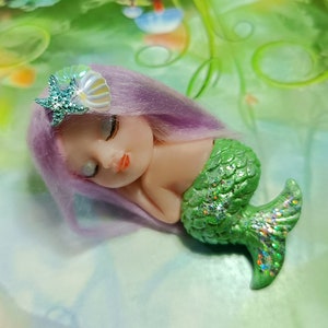 May include: A small, sleeping mermaid doll with purple hair and a green, glittery tail. She is wearing a seashell and starfish hair clip.