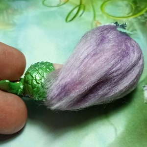 May include: A green mermaid figurine with a purple fuzzy tail. The mermaid has a crown and is made of plastic.