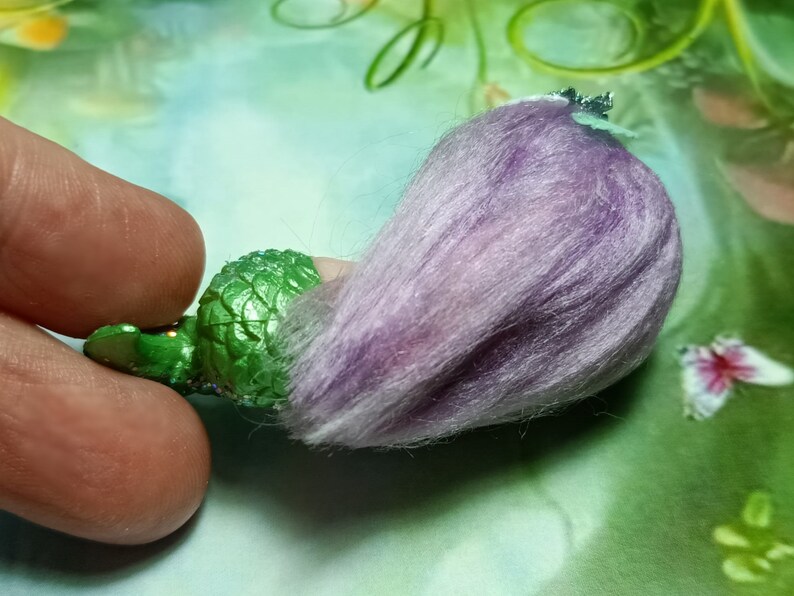 May include: A green mermaid figurine with a purple fuzzy tail. The mermaid has a crown and is made of plastic.