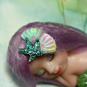 May include: A purple haired doll with a green glitter starfish and two iridescent seashell hair clips.