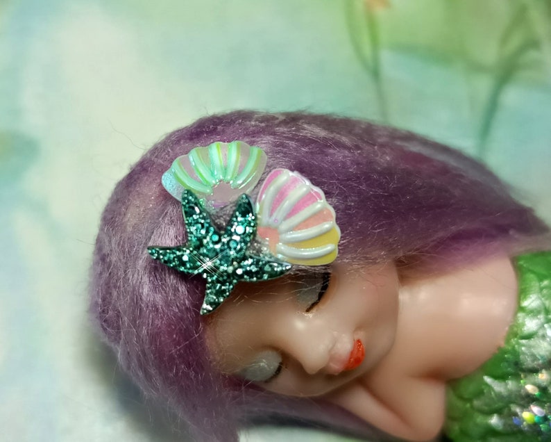 May include: A purple haired doll with a green glitter starfish and two iridescent seashell hair clips.