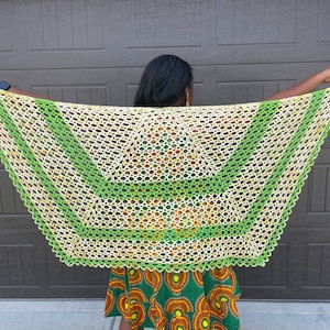 Peut inclure: Une femme portant un châle crocheté vert et blanc avec un motif géométrique. Le châle est drapé sur ses épaules et est maintenu en place par ses mains.