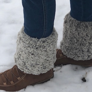 May include: A pair of brown leather boots with gray faux fur leg warmers. The boots are worn and the leg warmers are slightly wrinkled.