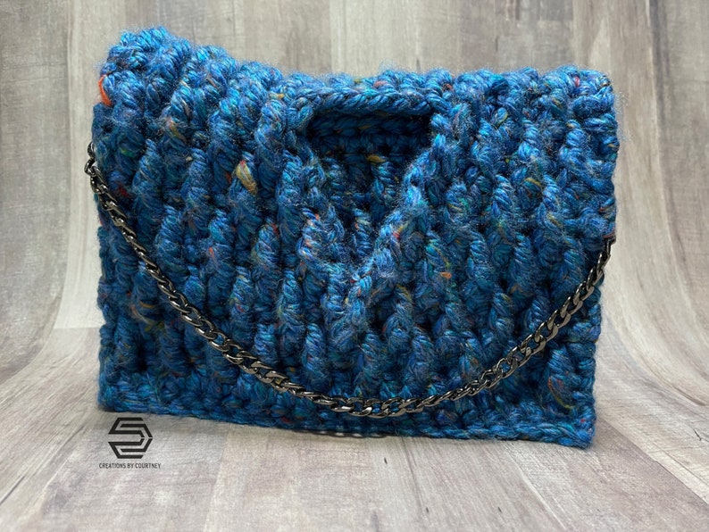 May include: A blue crocheted handbag with a silver chain strap. The bag has a textured, chunky knit design and is made with a speckled yarn.