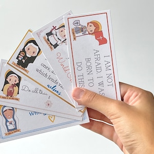 May include: Five colorful cards with illustrations of saints and inspirational quotes. The quotes include "I am not afraid. I was born to do this." and "World on ones, a... which lends va... actions. Do all that..."
