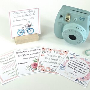 Peut inclure: Quatre cartes de citations inspirantes avec des motifs floraux et un appareil photo instantané bleu clair. Les citations portent sur la gentillesse, l'amour et le pardon. Les cartes sont sur une surface blanche.