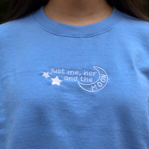 Puede incluir: Una sudadera azul claro con bordado blanco que dice "just me, her and the MOON" con dos estrellas sobre el texto.