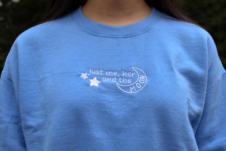 Puede incluir: Una sudadera azul claro con bordado blanco que dice "just me, her and the MOON" con dos estrellas sobre el texto.