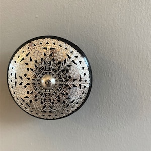 May include: A black and silver decorative round ornament with an intricate design. The ornament has a silver filigree pattern with a central star shape.