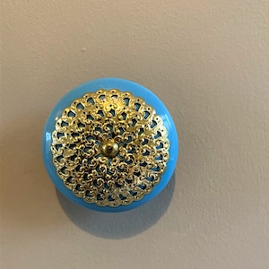May include: A light blue round cabinet knob with a gold filigree design.