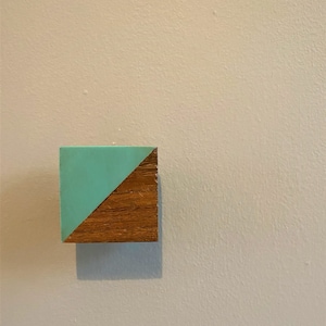 May include: A square wooden block with a diagonal line dividing it in half. One half is painted a light teal blue, and the other half is a natural wood colour.