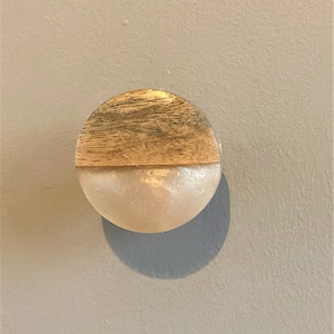 May include: A round wooden and white knob with a natural wood grain pattern on the top half.