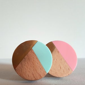 May include: Two round wooden knobs with a geometric design. One knob is painted light blue and gold, the other is painted pink and gold.