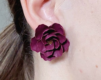 May include: A single, dark burgundy flower-shaped earring. The earring is a detailed replica of a peony, with multiple layers of petals and a golden center. The earring is worn on the ear, with the post hidden from view.